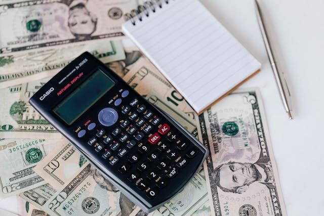 A calculator, a notebook, and some American money.