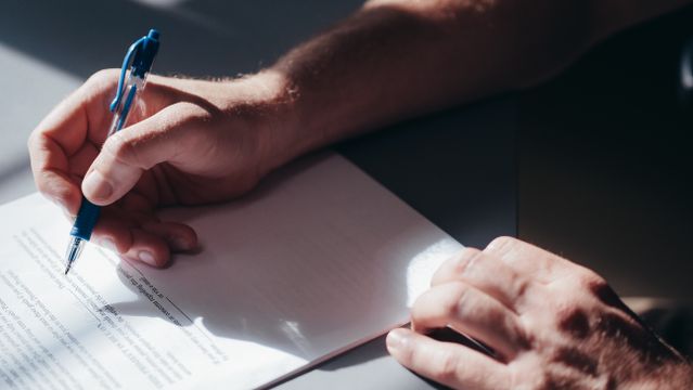 hand signing a document with a blue pen